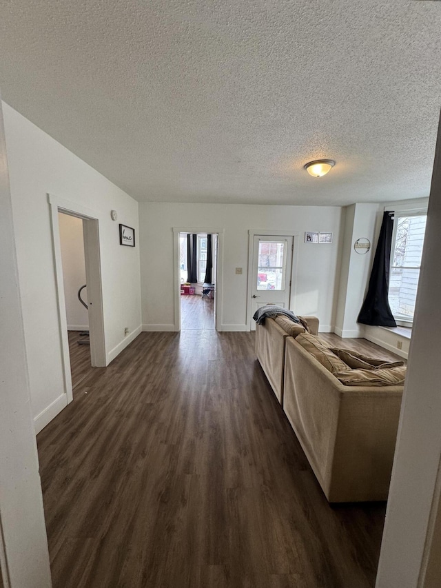 unfurnished living room featuring dark wood-style flooring, a textured ceiling, and baseboards