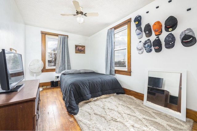 bedroom with hardwood / wood-style flooring, baseboards, ceiling fan, and a textured ceiling