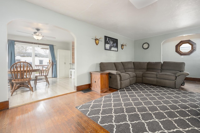 living area featuring arched walkways, baseboards, a ceiling fan, and wood-type flooring