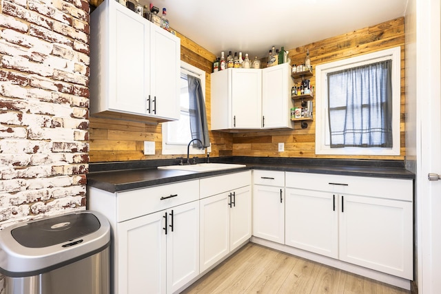 kitchen featuring white cabinets, a sink, dark countertops, and light wood-style flooring