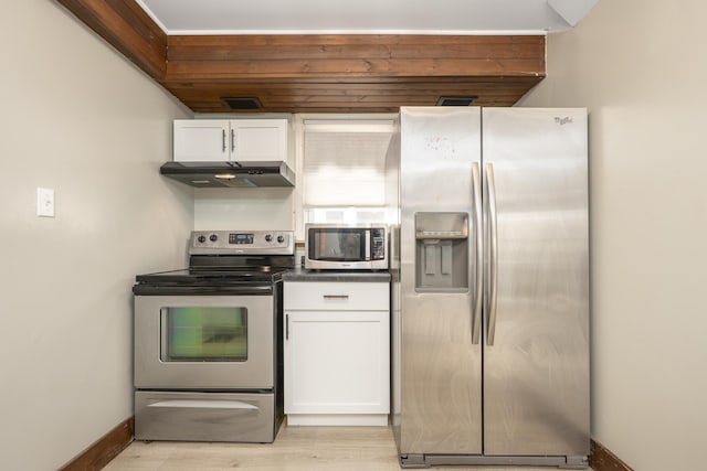 kitchen with white cabinets, dark countertops, appliances with stainless steel finishes, under cabinet range hood, and light wood-type flooring