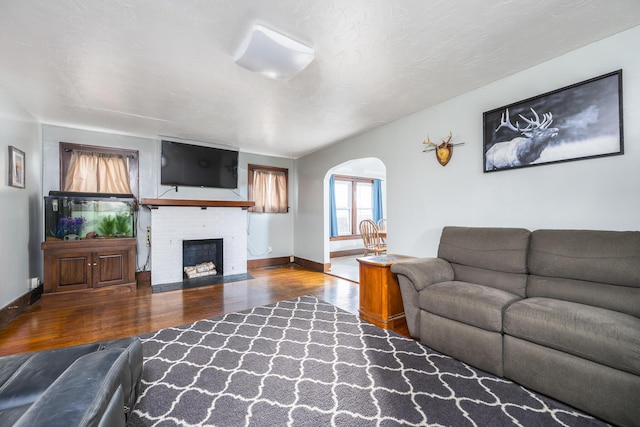 living room featuring arched walkways, baseboards, a fireplace, and wood finished floors