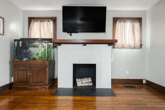 unfurnished living room featuring baseboards, a wealth of natural light, wood finished floors, and a brick fireplace