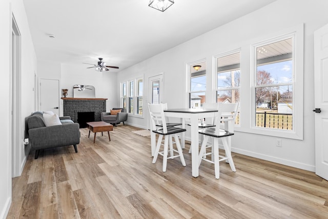 dining space featuring baseboards, light wood-style floors, a brick fireplace, and ceiling fan