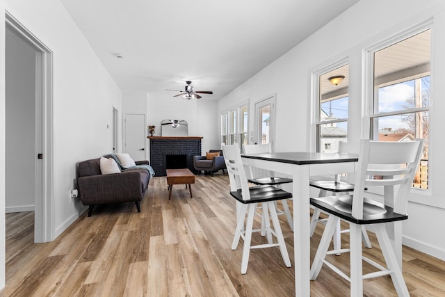 dining space featuring plenty of natural light, light wood-style floors, a brick fireplace, and a ceiling fan