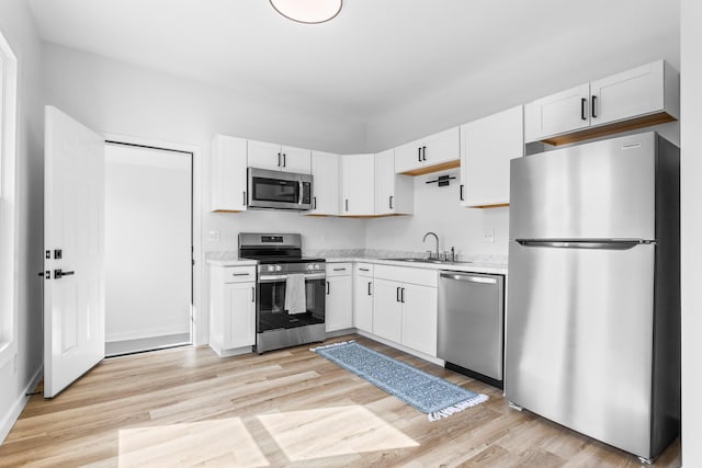 kitchen featuring a sink, stainless steel appliances, light countertops, white cabinetry, and light wood-type flooring