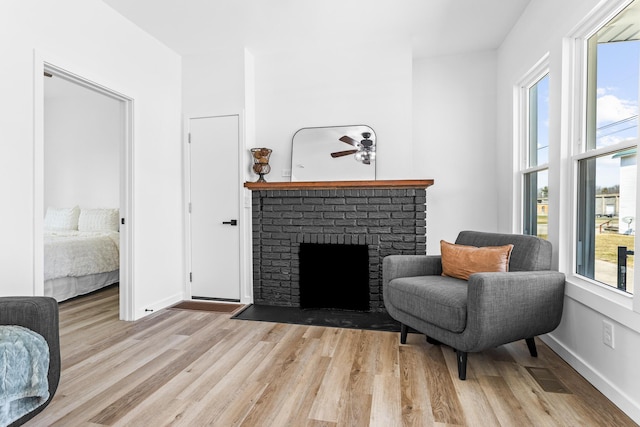 living area featuring light wood-type flooring, visible vents, baseboards, a brick fireplace, and ceiling fan