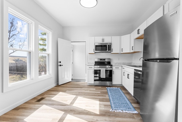 kitchen with white cabinetry, stainless steel appliances, light countertops, and light wood-style floors