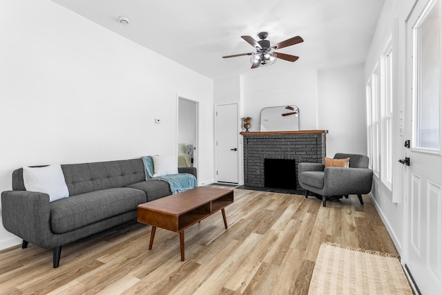 living area featuring a fireplace, light wood-style floors, baseboards, and ceiling fan