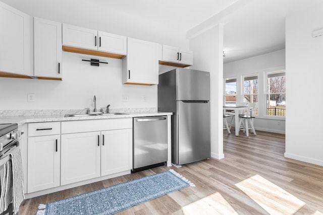 kitchen featuring baseboards, a sink, stainless steel appliances, white cabinetry, and light wood-type flooring