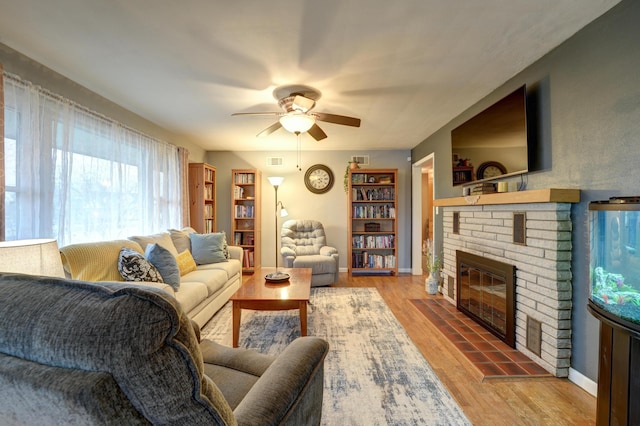 living area with a brick fireplace, light wood-style floors, visible vents, and ceiling fan