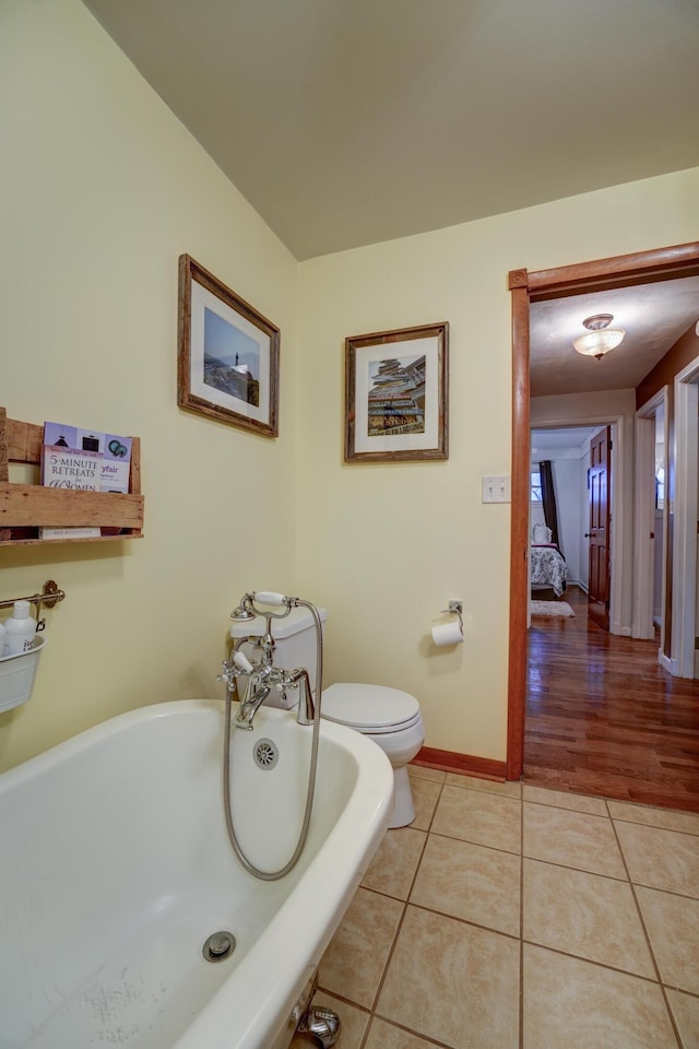 bathroom with tile patterned floors, baseboards, a soaking tub, and toilet