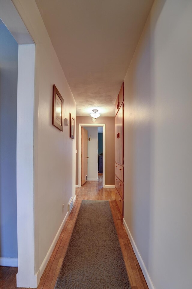 corridor featuring light wood-style flooring and baseboards