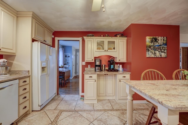 kitchen with light stone counters, cream cabinetry, white appliances, and glass insert cabinets