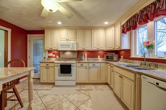 kitchen featuring a sink, light stone counters, cream cabinets, white appliances, and ceiling fan