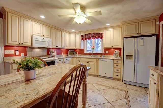 kitchen featuring cream cabinetry, a ceiling fan, light stone counters, a sink, and white appliances