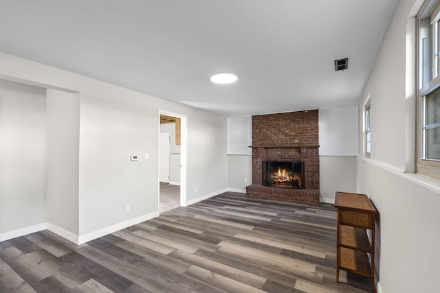unfurnished living room featuring a brick fireplace, baseboards, visible vents, and wood finished floors