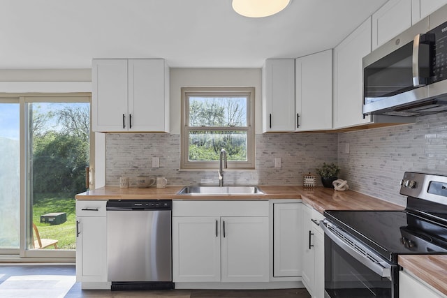kitchen with appliances with stainless steel finishes, butcher block counters, a sink, and plenty of natural light