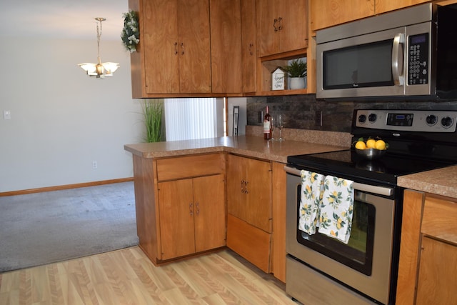 kitchen featuring pendant lighting, appliances with stainless steel finishes, backsplash, light hardwood / wood-style floors, and kitchen peninsula