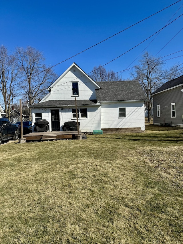 rear view of house with roof with shingles, a lawn, and a wooden deck