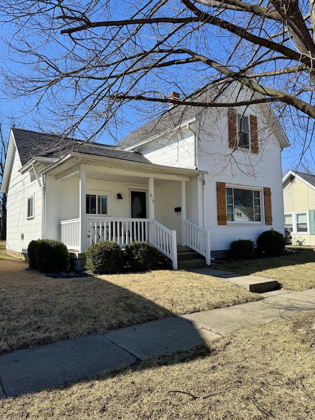 traditional-style house featuring a porch, a chimney, and a front lawn