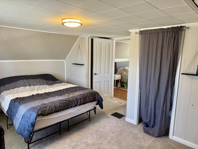 carpeted bedroom featuring visible vents and wooden walls