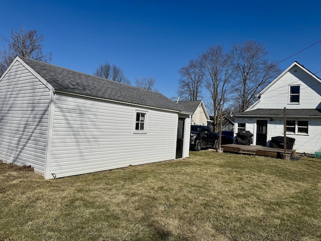 exterior space with an outbuilding, roof with shingles, a yard, and a wooden deck