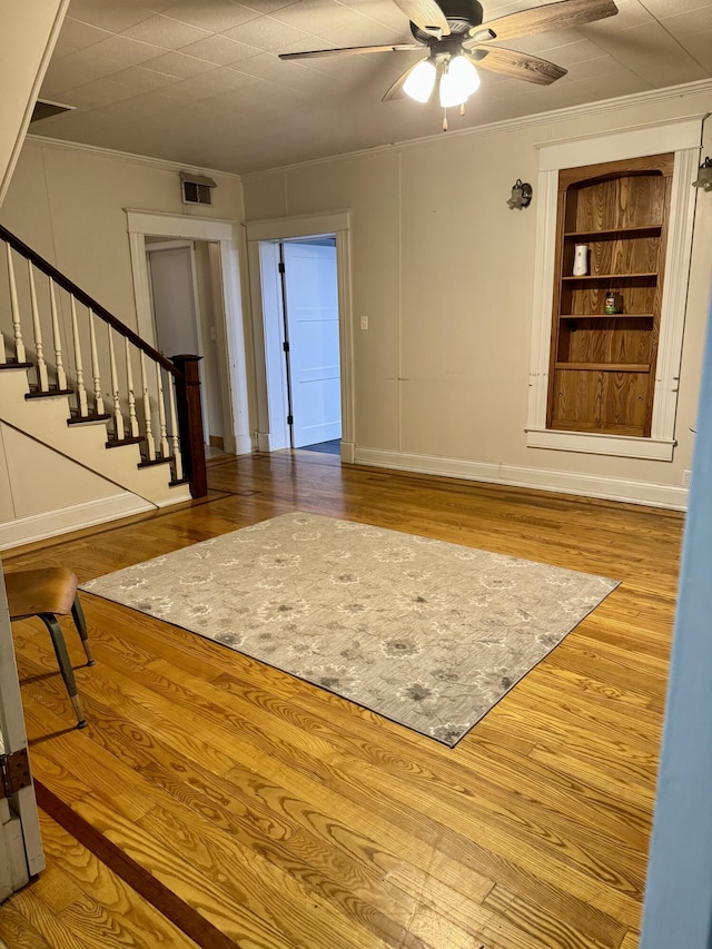 living room featuring built in shelves, ceiling fan, ornamental molding, and hardwood / wood-style floors