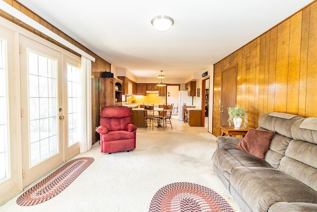 living area with french doors, light carpet, and wooden walls