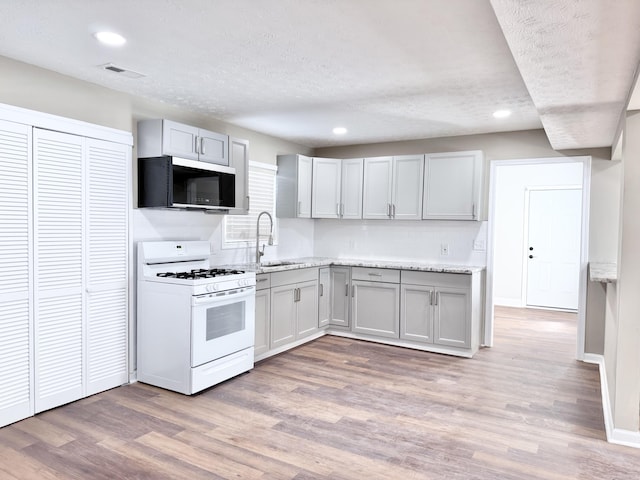 kitchen featuring sink, white gas stove, a textured ceiling, and light hardwood / wood-style flooring