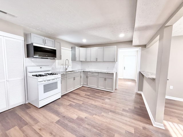 kitchen featuring white gas range, light hardwood / wood-style floors, sink, and a textured ceiling