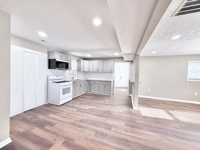 kitchen featuring sink, a textured ceiling, light wood-type flooring, and white gas range oven