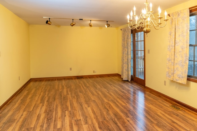 unfurnished room with an inviting chandelier, visible vents, baseboards, and wood finished floors