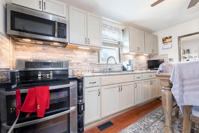 kitchen featuring visible vents, a sink, tasteful backsplash, wood finished floors, and stainless steel appliances