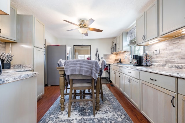 kitchen with a sink, backsplash, dark wood finished floors, stainless steel appliances, and ceiling fan