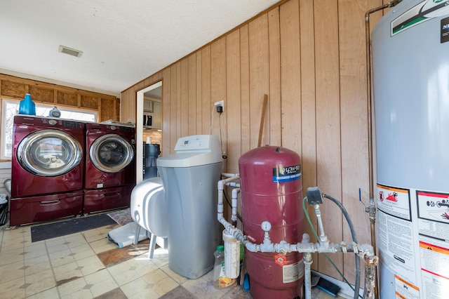 laundry room with wooden walls, laundry area, gas water heater, tile patterned floors, and washer and clothes dryer