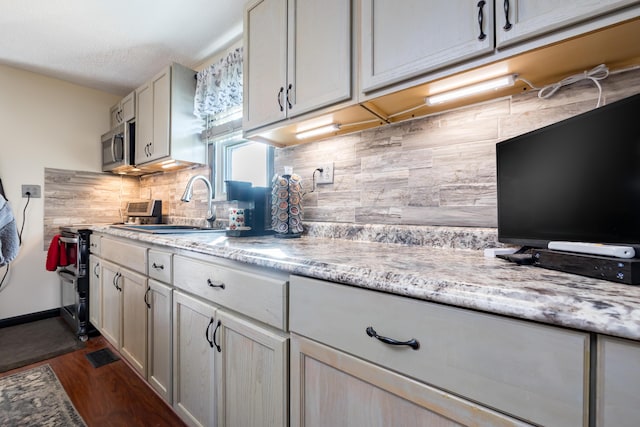 kitchen with backsplash, light stone counters, appliances with stainless steel finishes, dark wood-style floors, and a sink