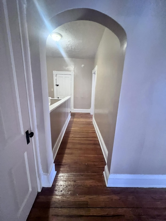 hallway featuring arched walkways, dark wood-style floors, and baseboards