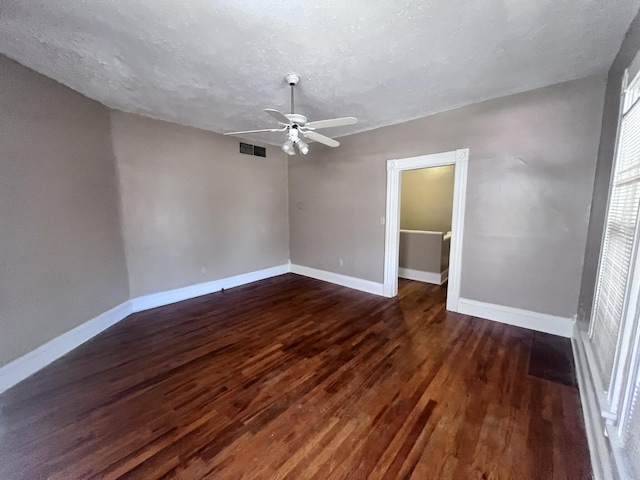 empty room featuring dark wood-style flooring, visible vents, and baseboards