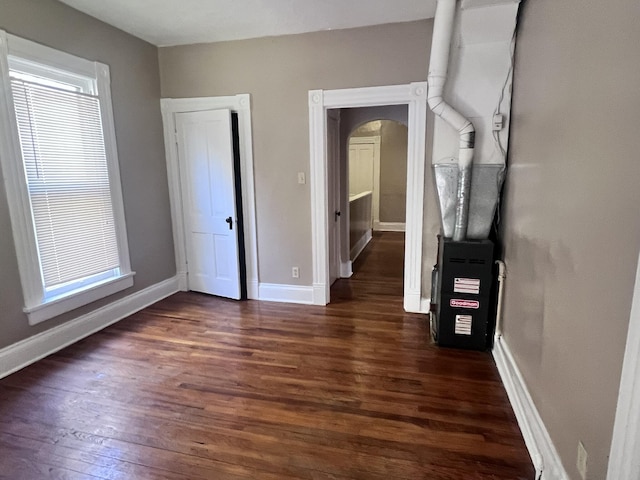 unfurnished bedroom with arched walkways, baseboards, and wood finished floors