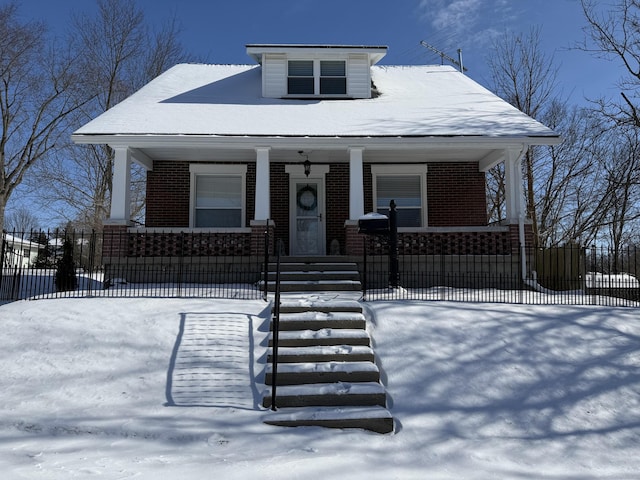 bungalow with covered porch, a fenced front yard, and brick siding