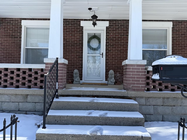 snow covered property entrance with brick siding