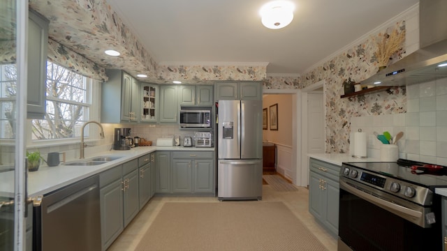 kitchen featuring gray cabinetry, ornamental molding, stainless steel appliances, wall chimney exhaust hood, and wallpapered walls