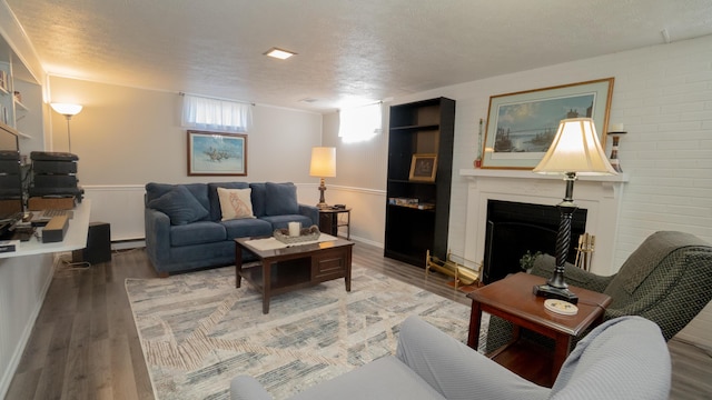 living area featuring a fireplace, wood finished floors, a baseboard heating unit, and a textured ceiling