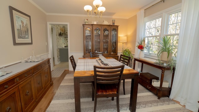 dining area featuring light wood-type flooring, wainscoting, a chandelier, and crown molding