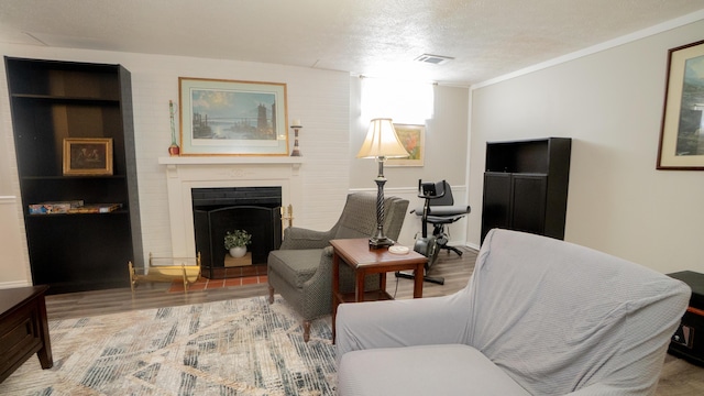 living area featuring wood finished floors, visible vents, a fireplace, ornamental molding, and a textured ceiling