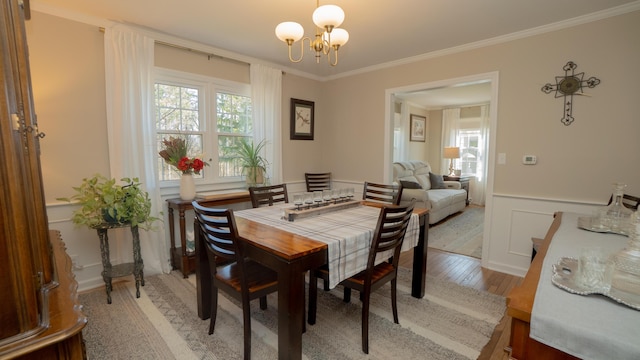 dining room with a wainscoted wall, light wood finished floors, an inviting chandelier, crown molding, and a decorative wall