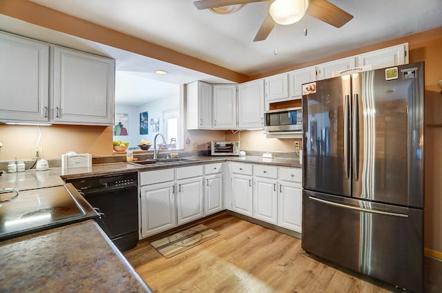 kitchen with stainless steel appliances, a sink, white cabinetry, light wood finished floors, and dark countertops