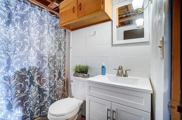 full bathroom featuring a shower with shower curtain, vanity, toilet, and concrete block wall