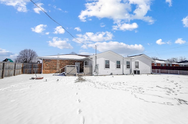 snow covered rear of property featuring central air condition unit, fence private yard, and brick siding